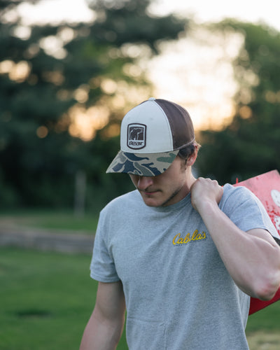 Man wearing a Bear Archery hat with Bear Archery logo and Fred Bear camo while carrying an archery target for bowhunting.