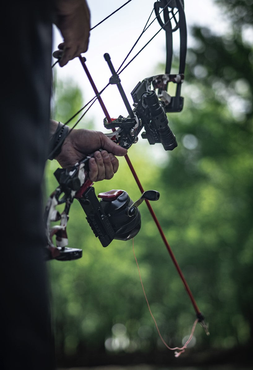 Cajun Bowfishing Bow equipped with a Cajun bowfishing reel and other bowfishing gear aimed into a body of water. 