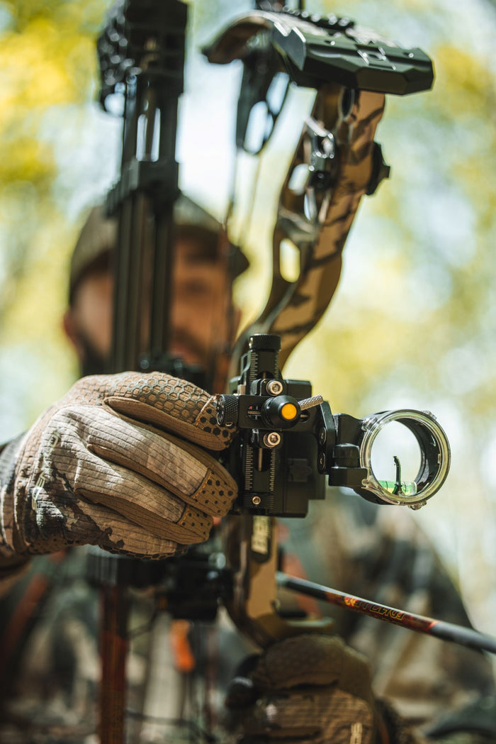 Man holding compound bow and tuning bow sight